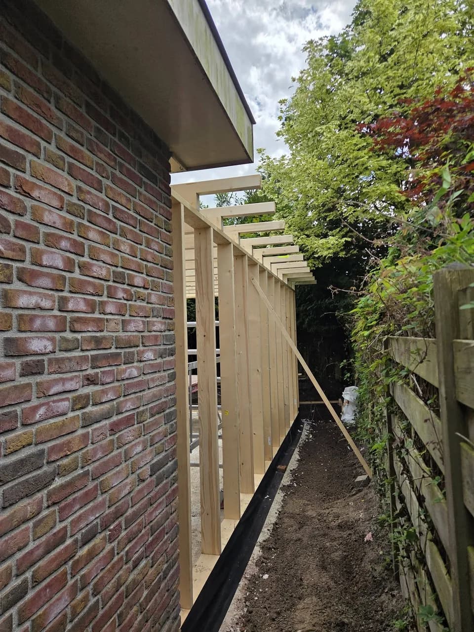 Zijaanzicht van het houten aanbouwframe langs de woning