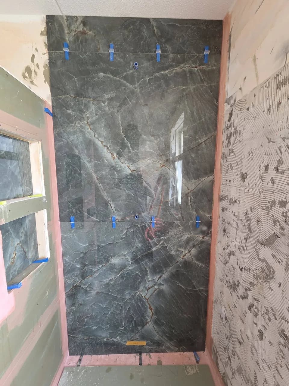 Marmerlook douchewand met tegelclips tijdens het tegelen